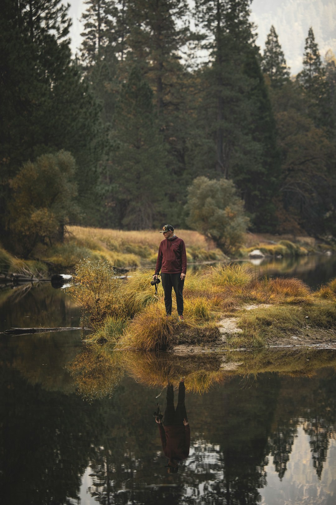 man in black jacket and black pants walking on green grass field near river during daytime