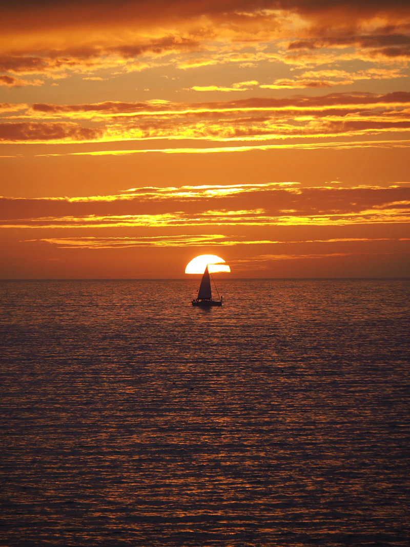 Sailboat silhouetted against a burning orange sunset at sea