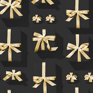A pattern of variously sized black gift boxes adorned with shiny golden ribbons, arranged neatly against a dark background. The lighting casts subtle shadows, highlighting the gleaming texture of the ribbons.