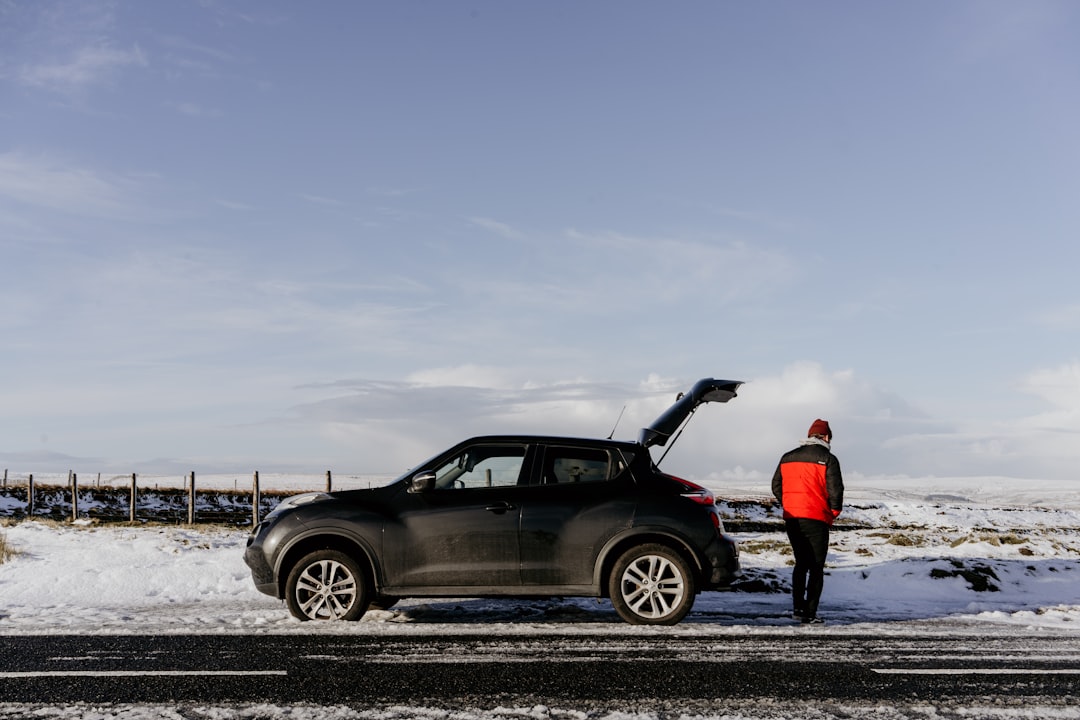 man in red jacket standing beside black sedan during daytime