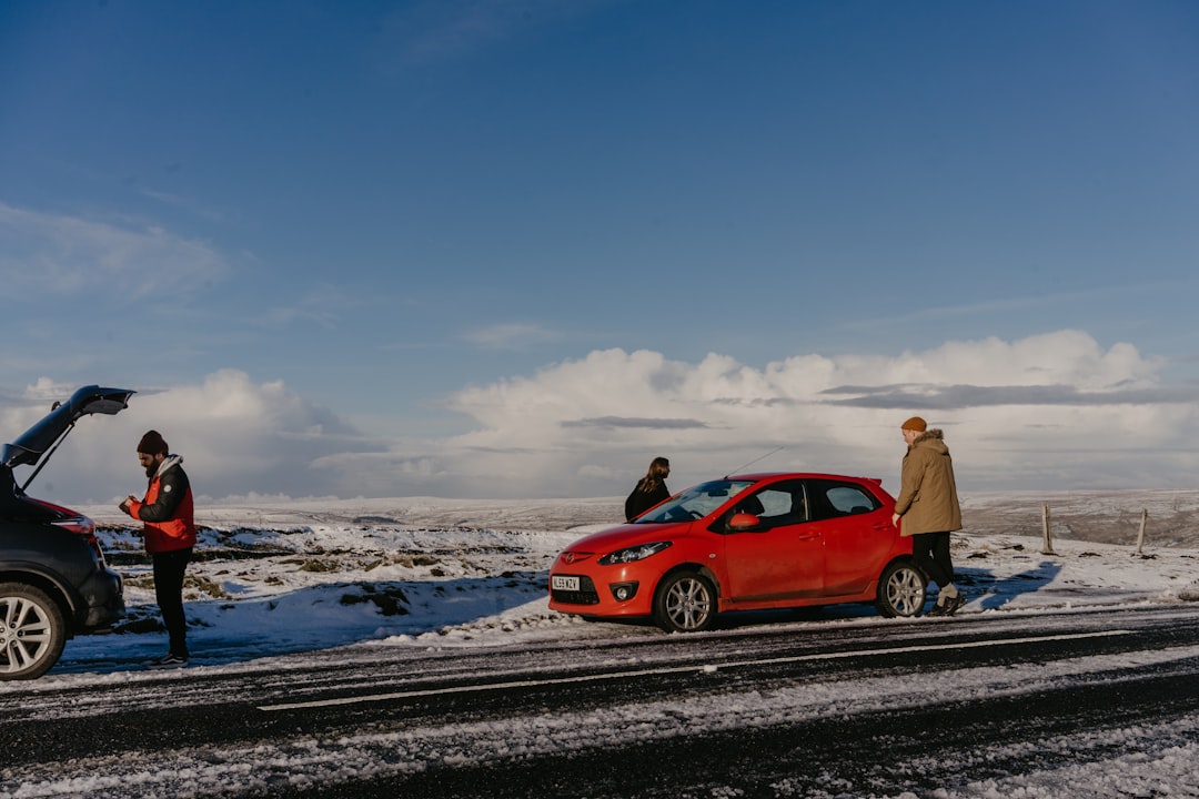 man in brown jacket standing beside red car on snow covered ground during daytime