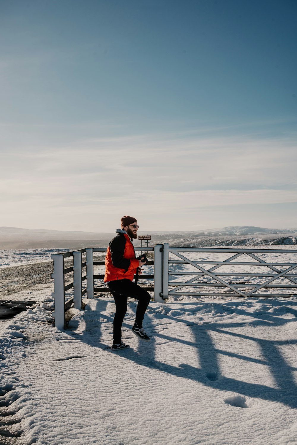 man in red jacket and black pants standing on gray wooden fence during daytime