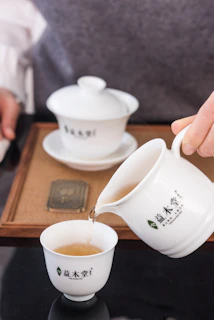 A traditional teapot pouring green tea into a small ceramic cup.