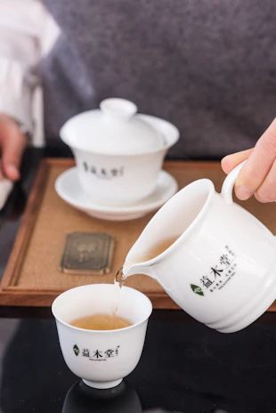 A traditional teapot pouring green tea into a small ceramic cup.