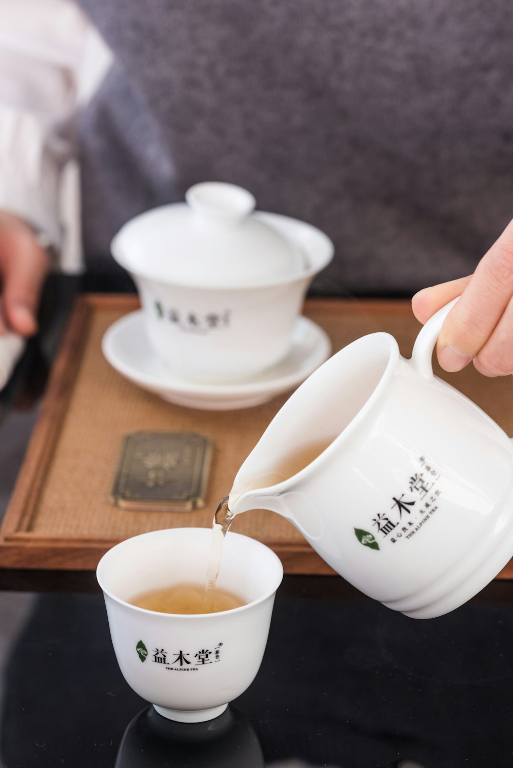 person pouring white ceramic teacup on brown wooden coaster