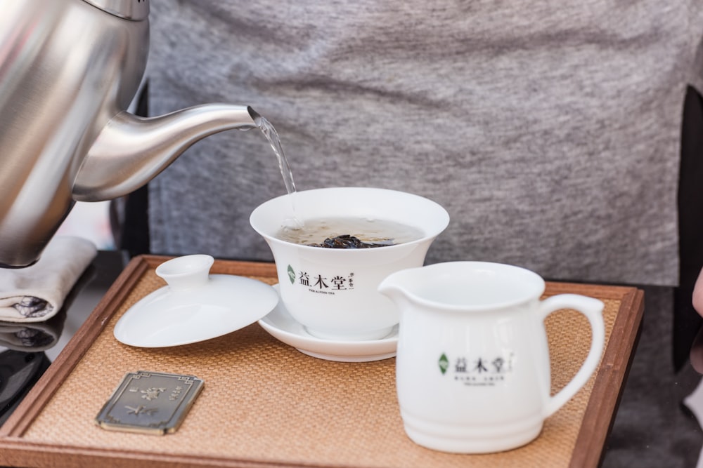 white ceramic teacup on saucer beside stainless steel teapot