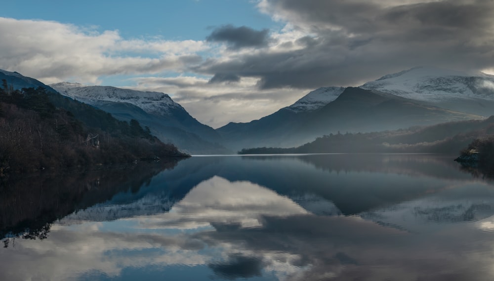 body of water near mountain under cloudy sky during daytime