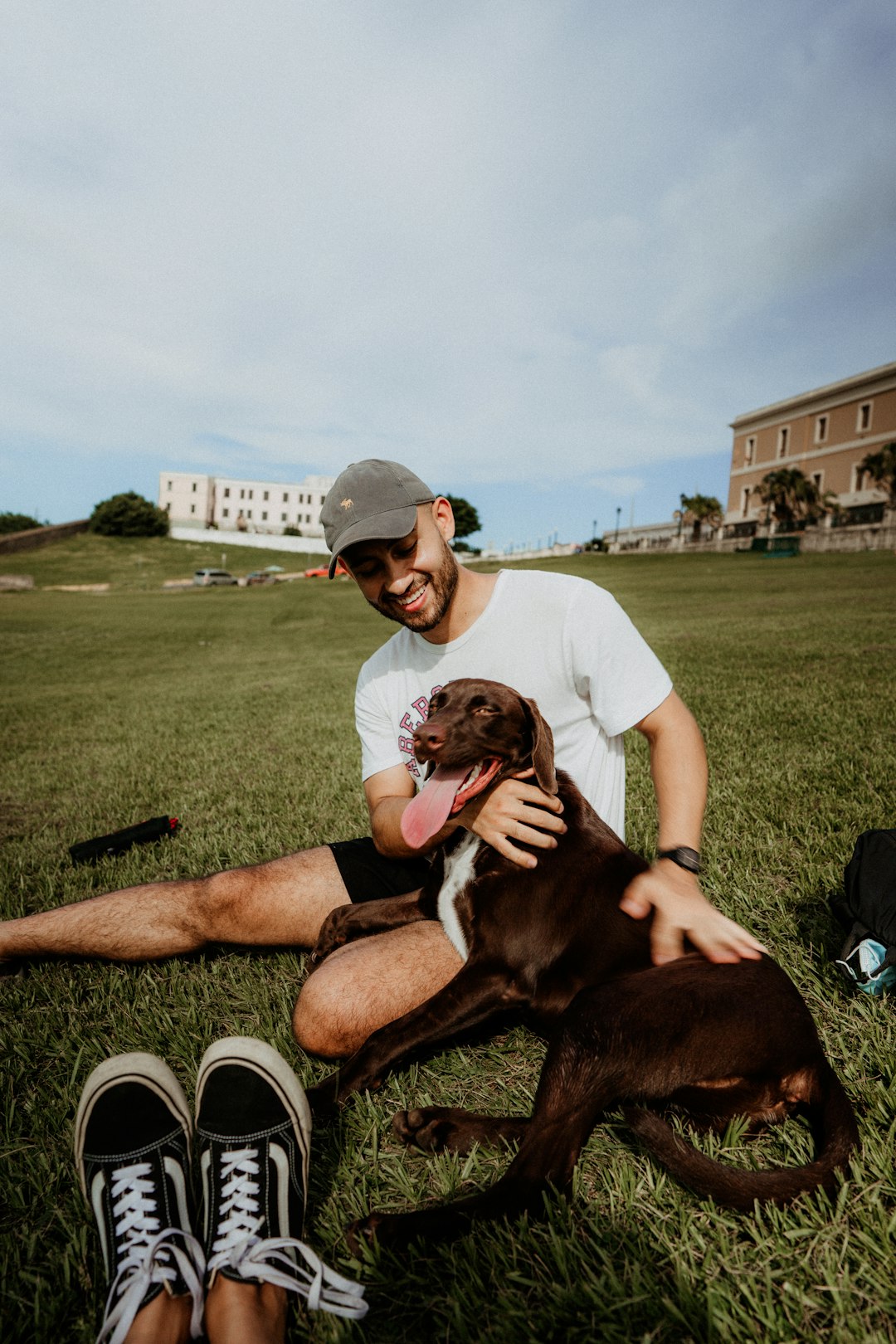 man in white crew neck t-shirt sitting on green grass field with brown short coated