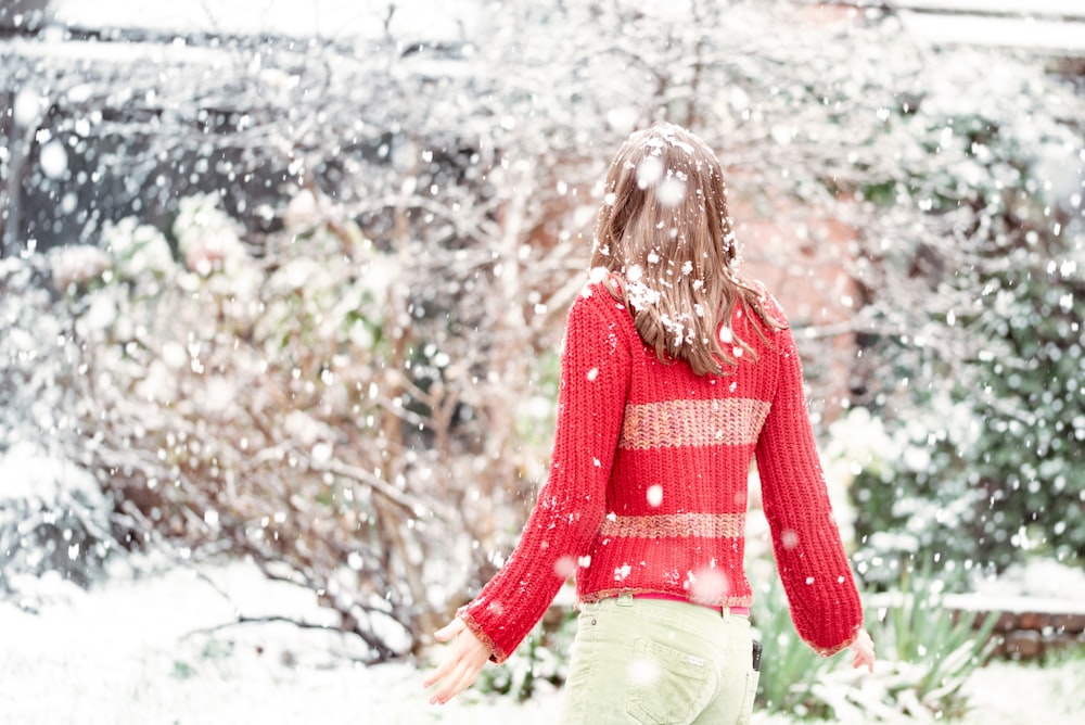 Mujer con suéter rojo y jeans de mezclilla blancos de pie en el suelo cubierto de nieve durante el día