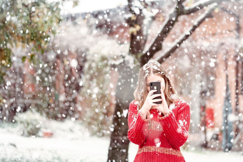woman in red sweater covering her face with silver and black camera