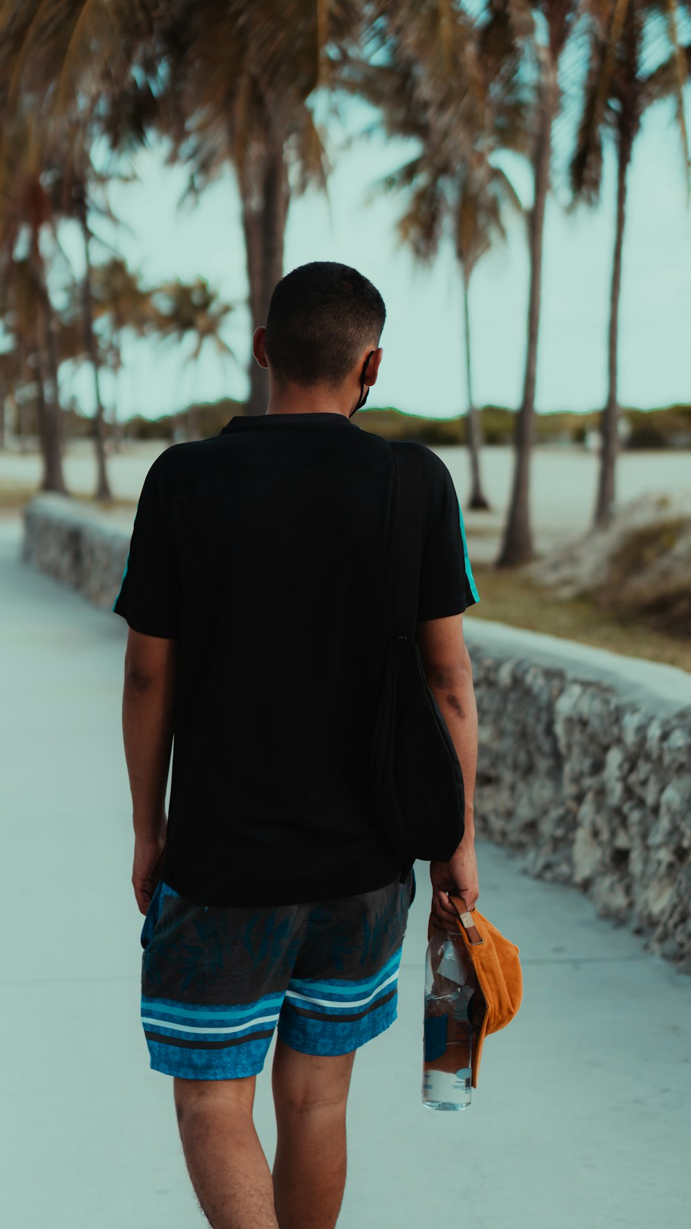 man in black crew neck t-shirt and blue denim shorts standing on gray concrete pavement