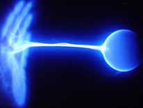 A bright blue plasma arc extends from the left to the right of the image, connecting two electrical nodes, possibly a Tesla coil or similar device. The plasma is luminous and appears to be sizzling with electrical energy.