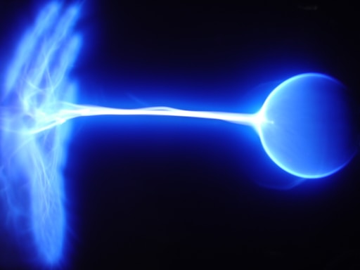 A bright blue plasma arc extends from the left to the right of the image, connecting two electrical nodes, possibly a Tesla coil or similar device. The plasma is luminous and appears to be sizzling with electrical energy.