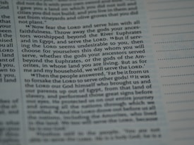 The image contains a close-up section of a book, likely a religious text, with slightly blurred and highlighted text emphasizing the words 'Lord', 'serve', and 'choose'. The text appears structured in paragraphs with some sections indented.