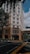 A tall building with a modern design, featuring a hospital entrance on the ground floor. The street intersection in front has traffic markings and a pedestrian crossing. Trees and parked vehicles are present, contributing to an urban environment.