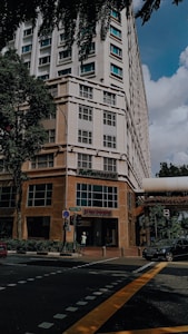 A tall building with a modern design, featuring a hospital entrance on the ground floor. The street intersection in front has traffic markings and a pedestrian crossing. Trees and parked vehicles are present, contributing to an urban environment.