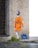 A stencil-style street art depicts a child with grey hair facing away, wearing an orange raincoat with the words 'Sea Rescue is not a crime' printed on the back. The child pulls a blue toy boat on a string. The artwork is painted on a textured concrete wall next to a darker brick wall, with grass and pavement visible below.