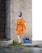 A stencil-style street art depicts a child with grey hair facing away, wearing an orange raincoat with the words 'Sea Rescue is not a crime' printed on the back. The child pulls a blue toy boat on a string. The artwork is painted on a textured concrete wall next to a darker brick wall, with grass and pavement visible below.