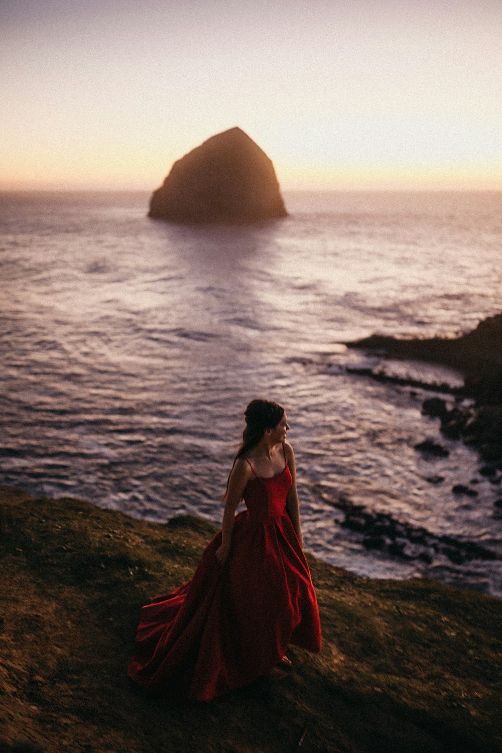 woman in red dress standing on rock near body of water during daytime