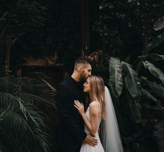 man and woman kissing near green plants during daytime