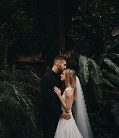 man and woman kissing near green plants during daytime