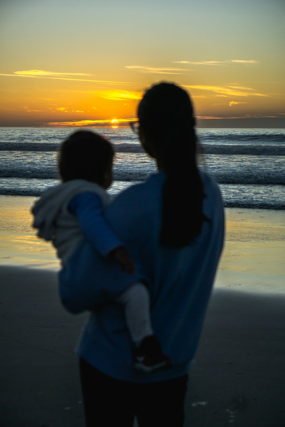 mulher na camisa branca da manga comprida em pé na praia durante o pôr do sol