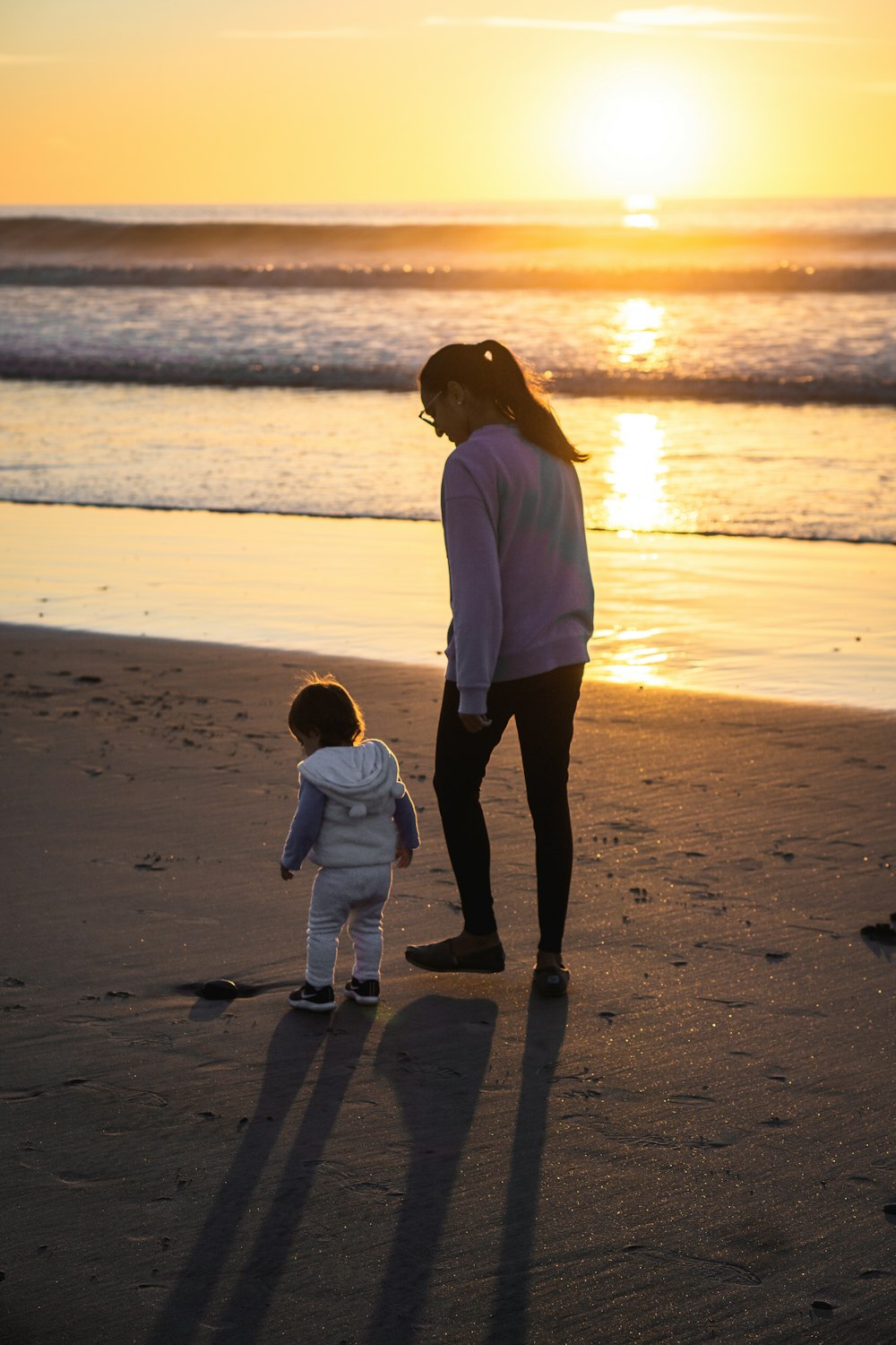 Mujer con camisa blanca de manga larga y pantalones negros caminando en la playa durante el día