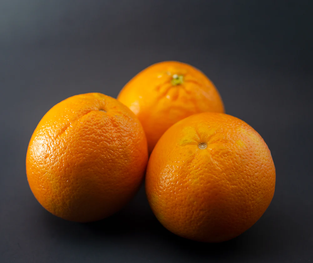 Two oranges resting on a black surface, lit warm and low.
