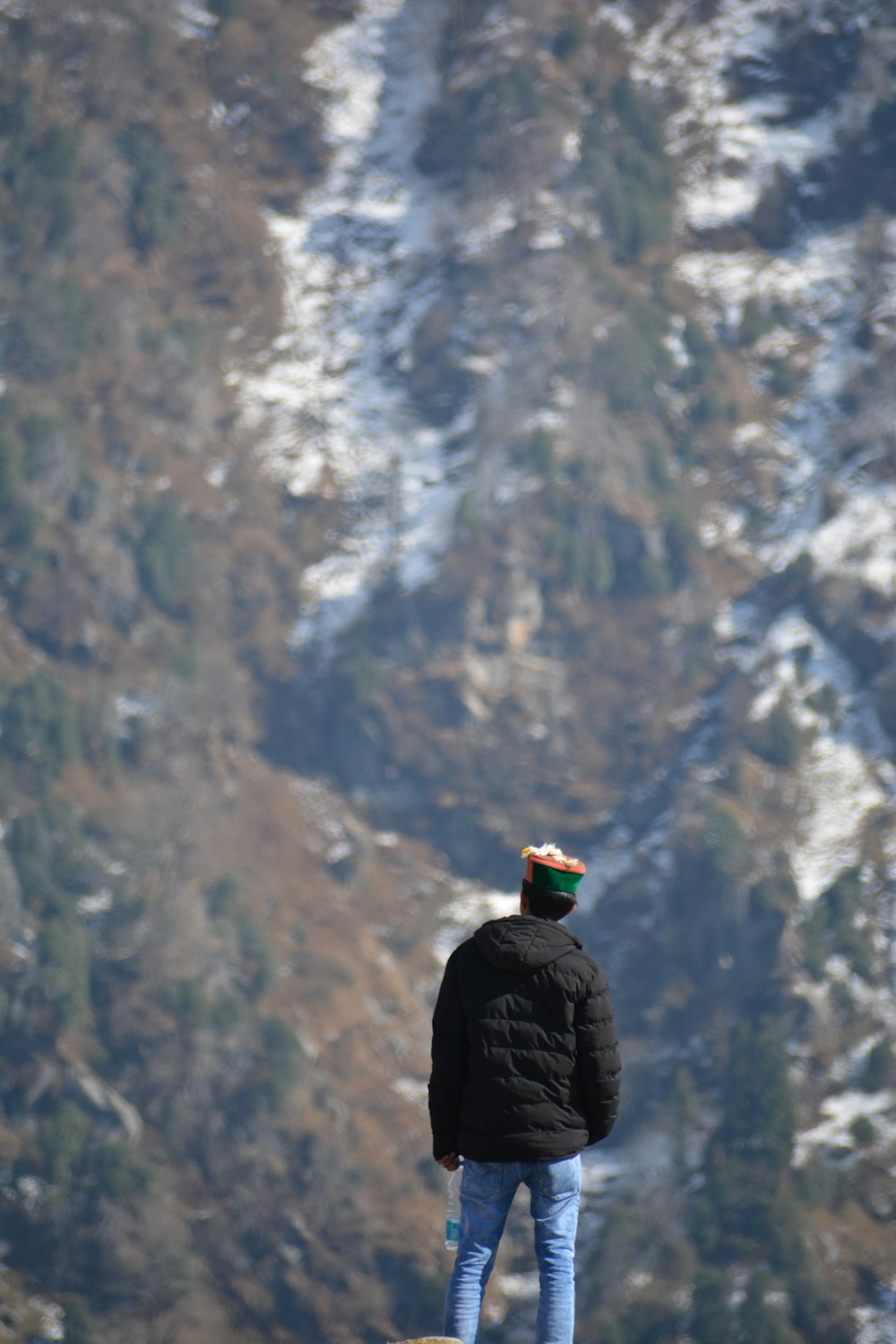 Person in schwarzer Jacke, die tagsüber auf einer Felsformation steht und auf den schneebedeckten Berg blickt