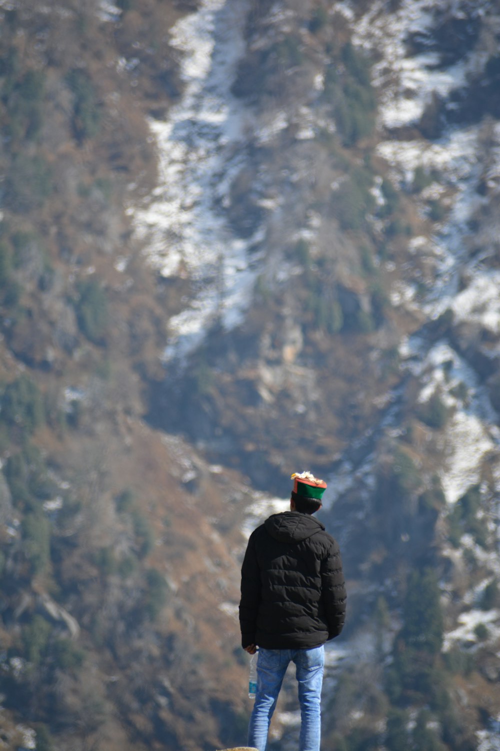 person in black jacket standing on rock formation looking at snow covered mountain during daytime