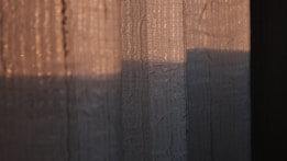 The image captures a close-up view of textured fabric with a play of light and shadow. The fabric appears semi-transparent with visible patterns, likely from natural fiber, illuminated by warm, diffused sunlight.
