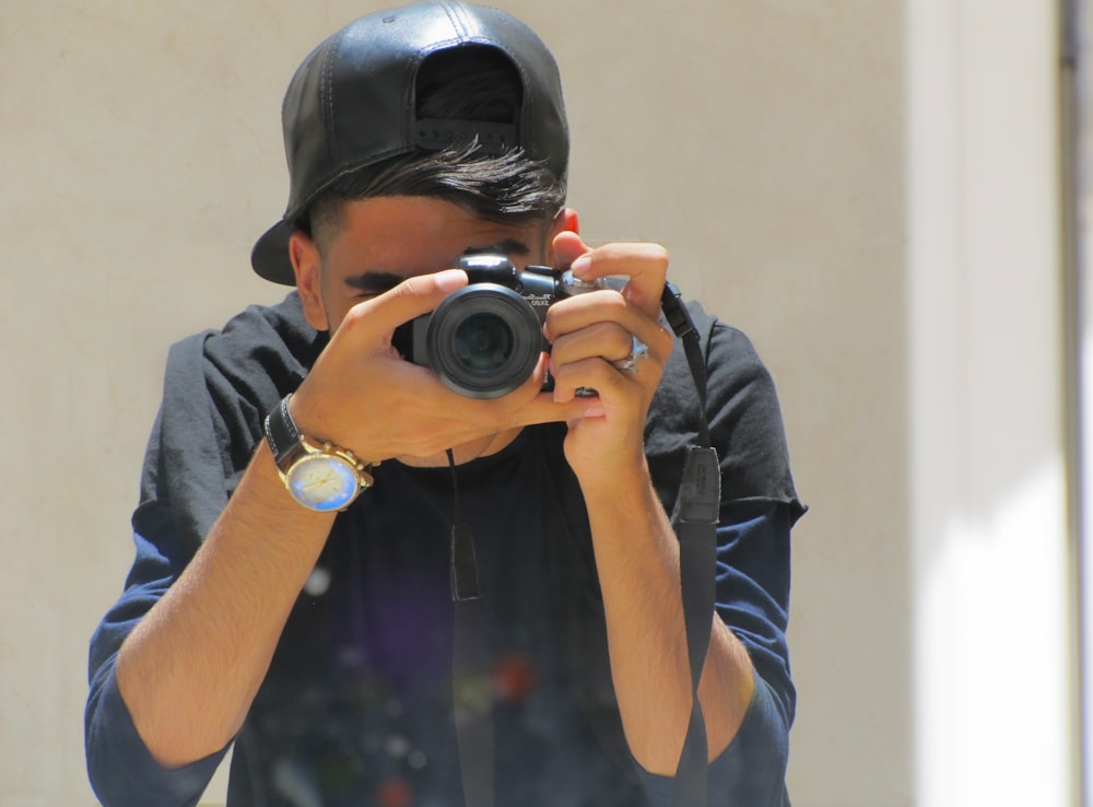 man in black cap holding black dslr camera