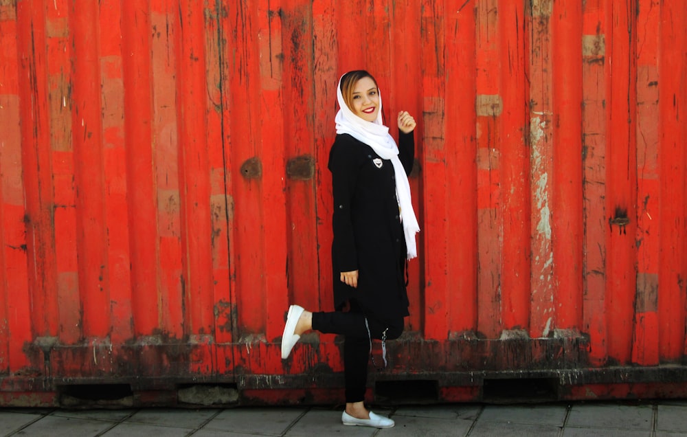 woman in black blazer and white shirt standing beside red wooden wall