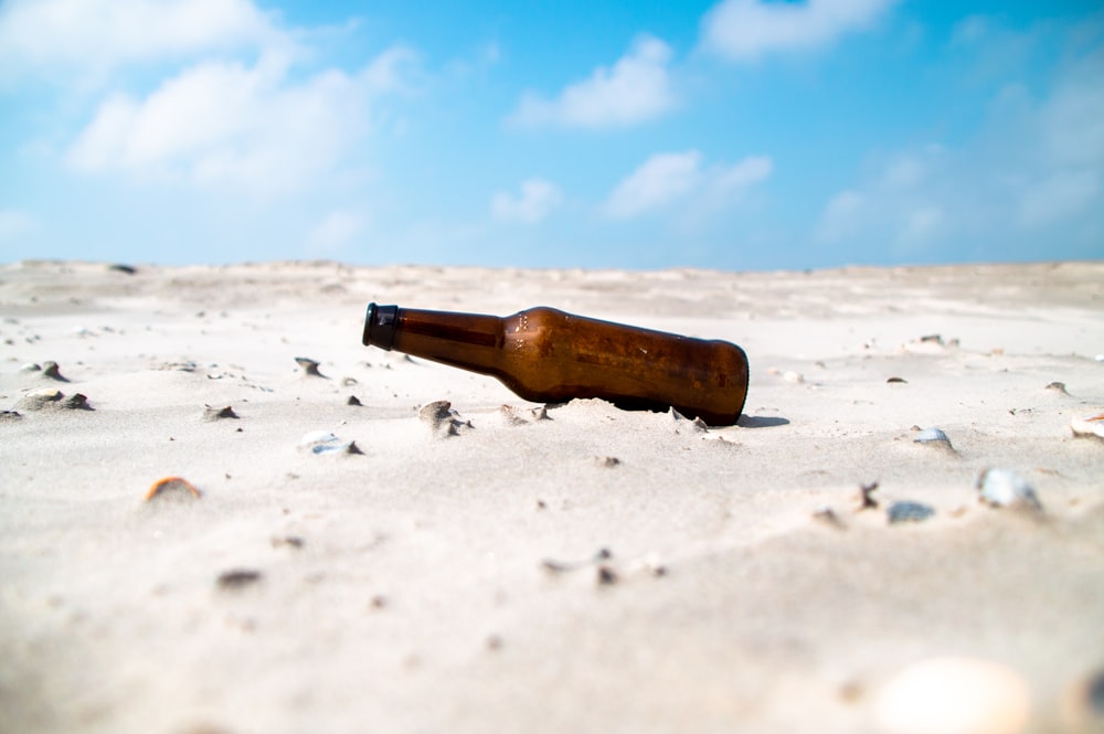 bouteille en verre brun sur sable blanc pendant la journée