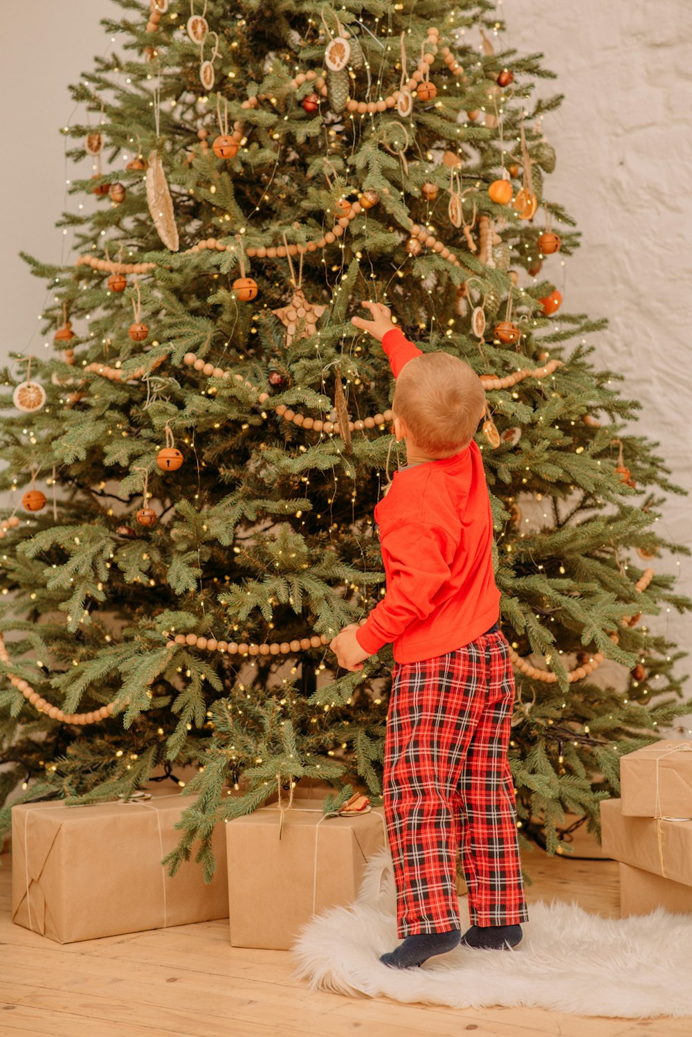 boy in red long sleeve shirt standing beside green christmas tree