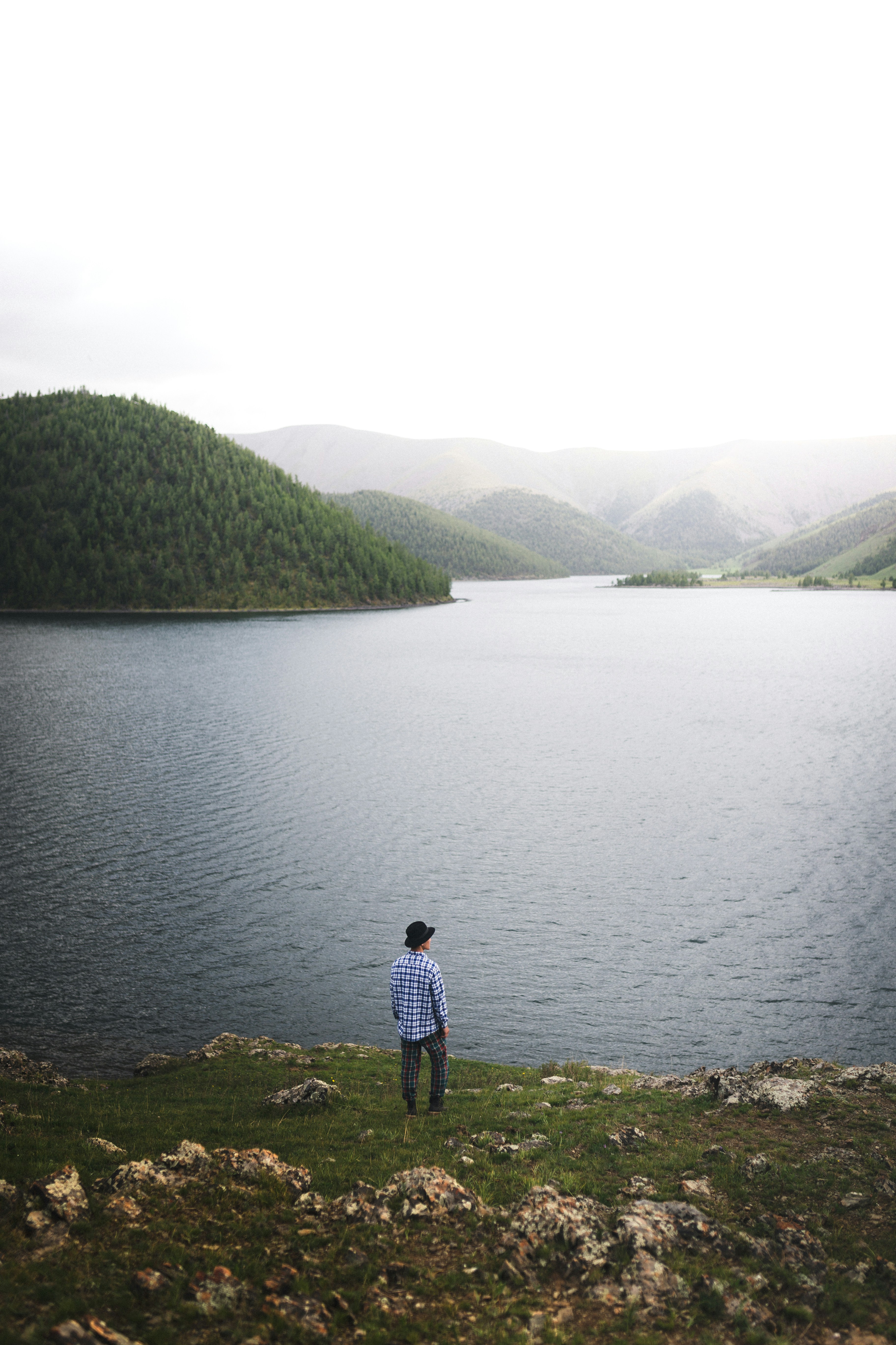 man in black jacket standing on green grass near lake during daytime