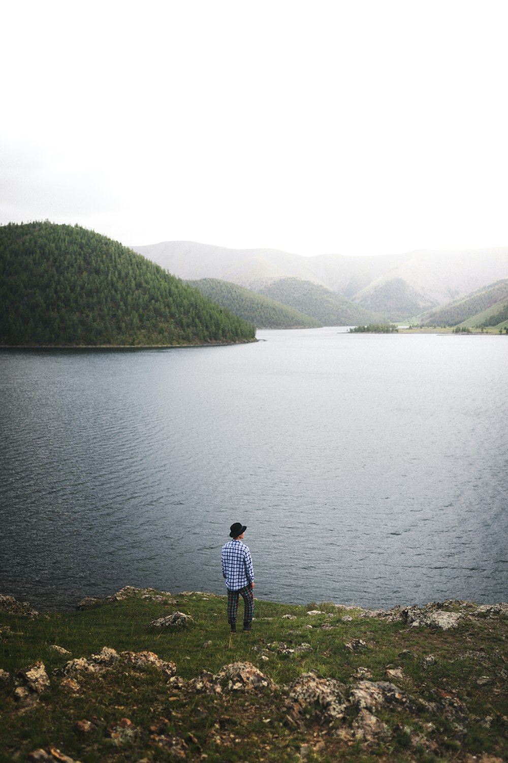 man in black jacket standing on green grass near lake during daytime