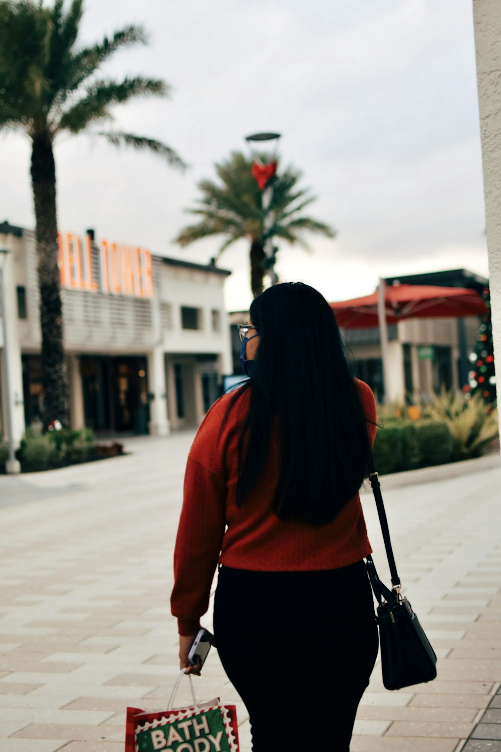 woman in red long sleeve shirt and black skirt standing on sidewalk during daytime