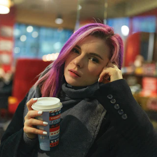 A woman wearing elegant purple gloves while holding a coffee cup in a cozy café setting.