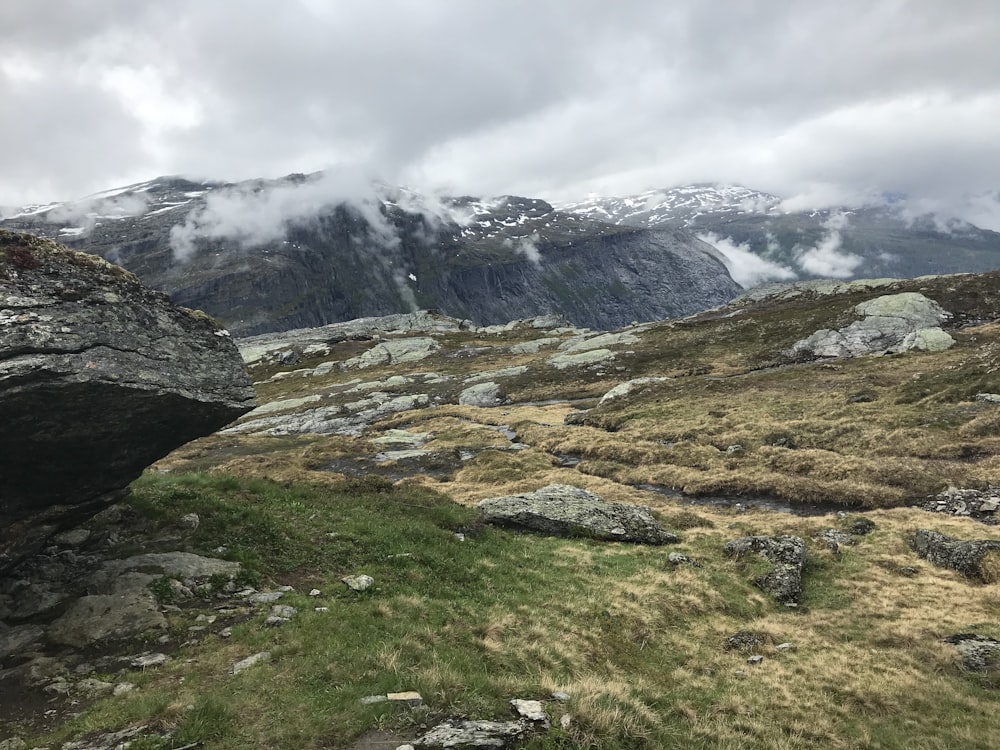 campo de grama verde perto da montanha sob nuvens brancas durante o dia