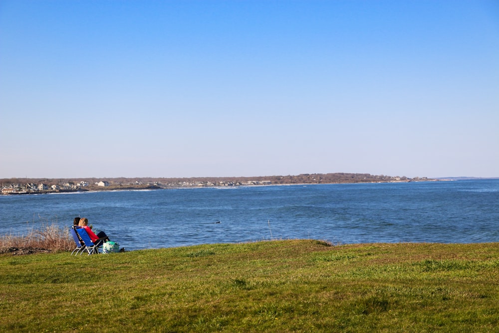 people sitting on green grass field near body of water during daytime