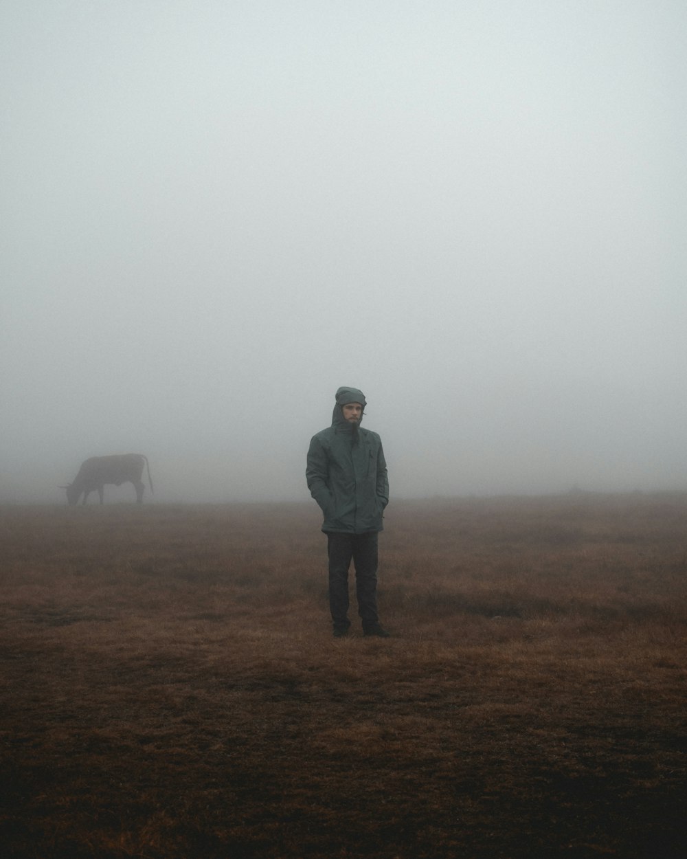 man in gray jacket standing on brown grass field