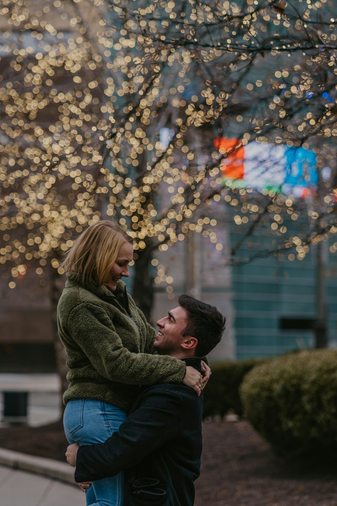 man and woman kissing under brown tree with string lights during daytime