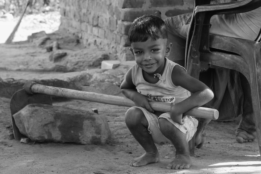 grayscale photo of boy in tank top sitting on concrete wall