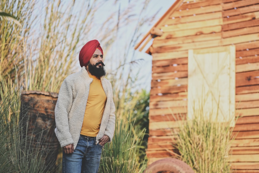 woman in beige cardigan and blue denim jeans standing near brown wooden house during daytime