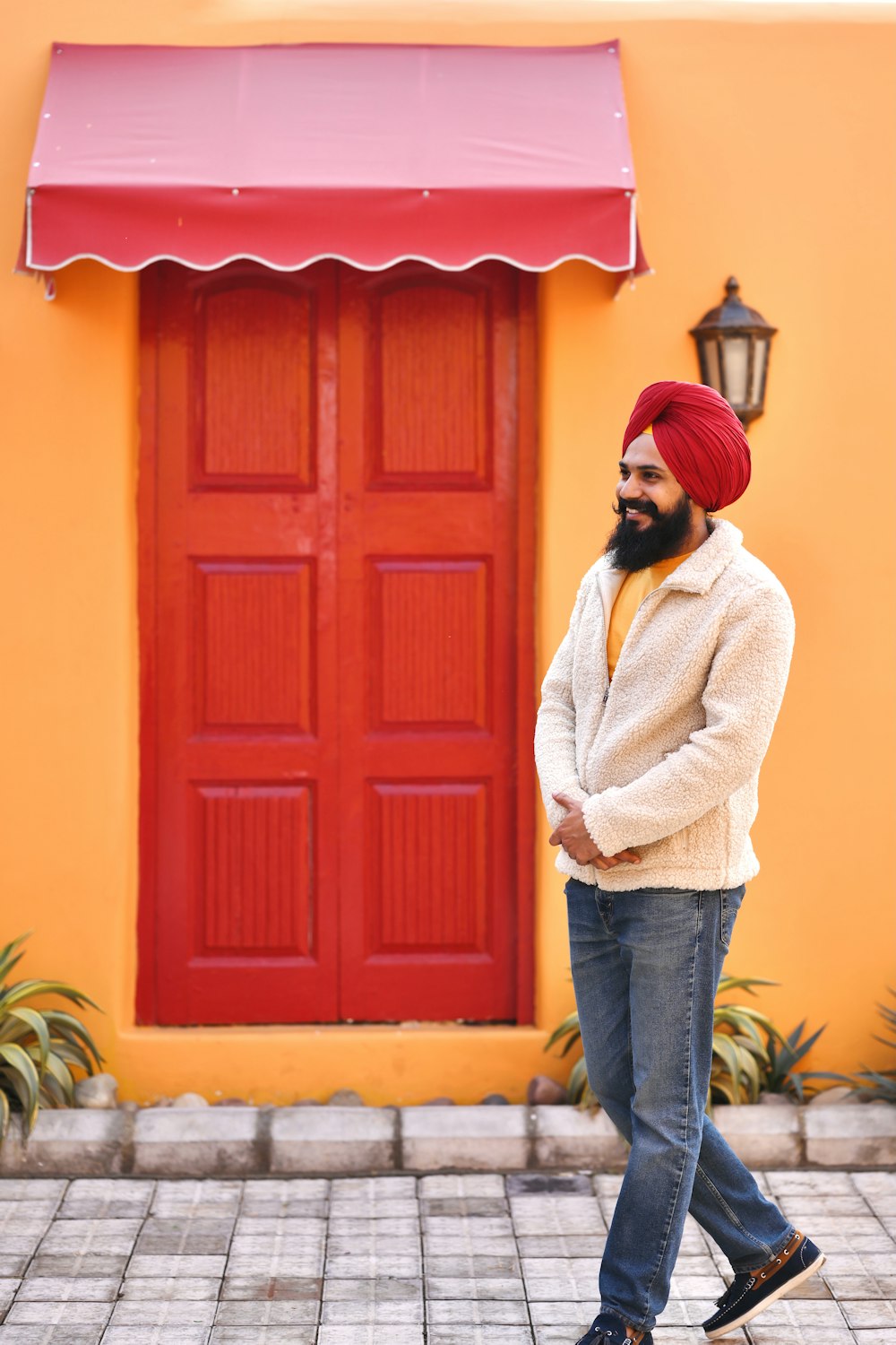 woman in white sweater and blue denim jeans standing beside red wooden door