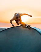 A skateboarder performing a trick on an urban ramp at sunset.