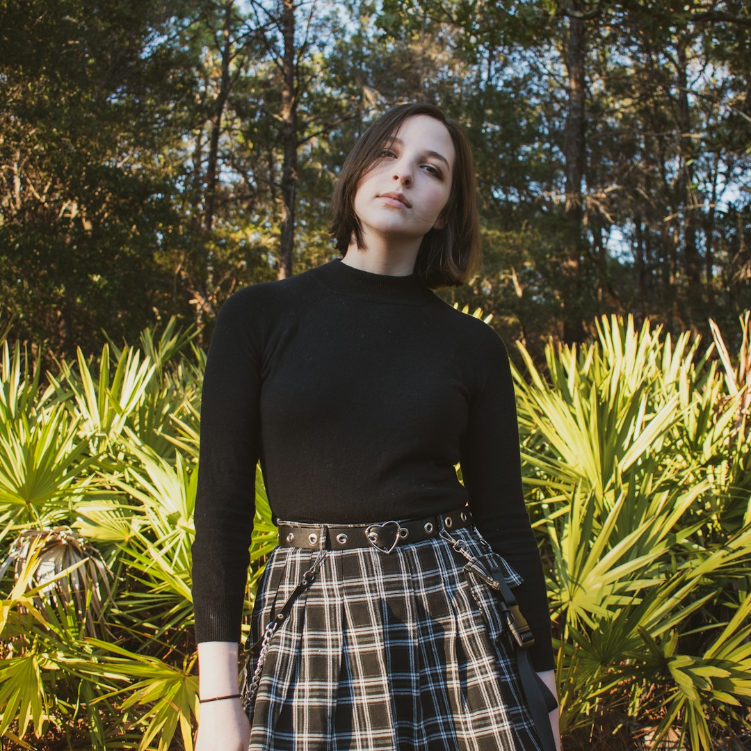woman in black long sleeve shirt and blue and white plaid skirt standing near green plants