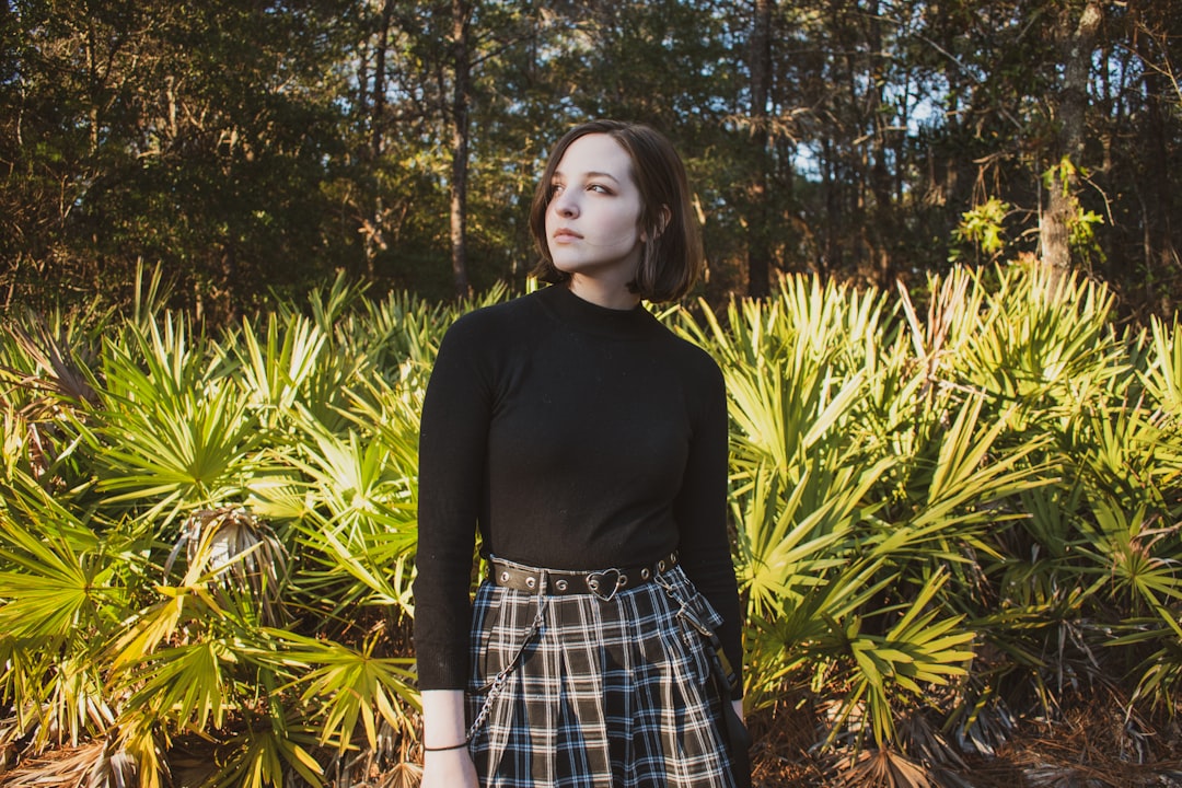 girl in black long sleeve shirt and blue and white plaid skirt standing near green plants