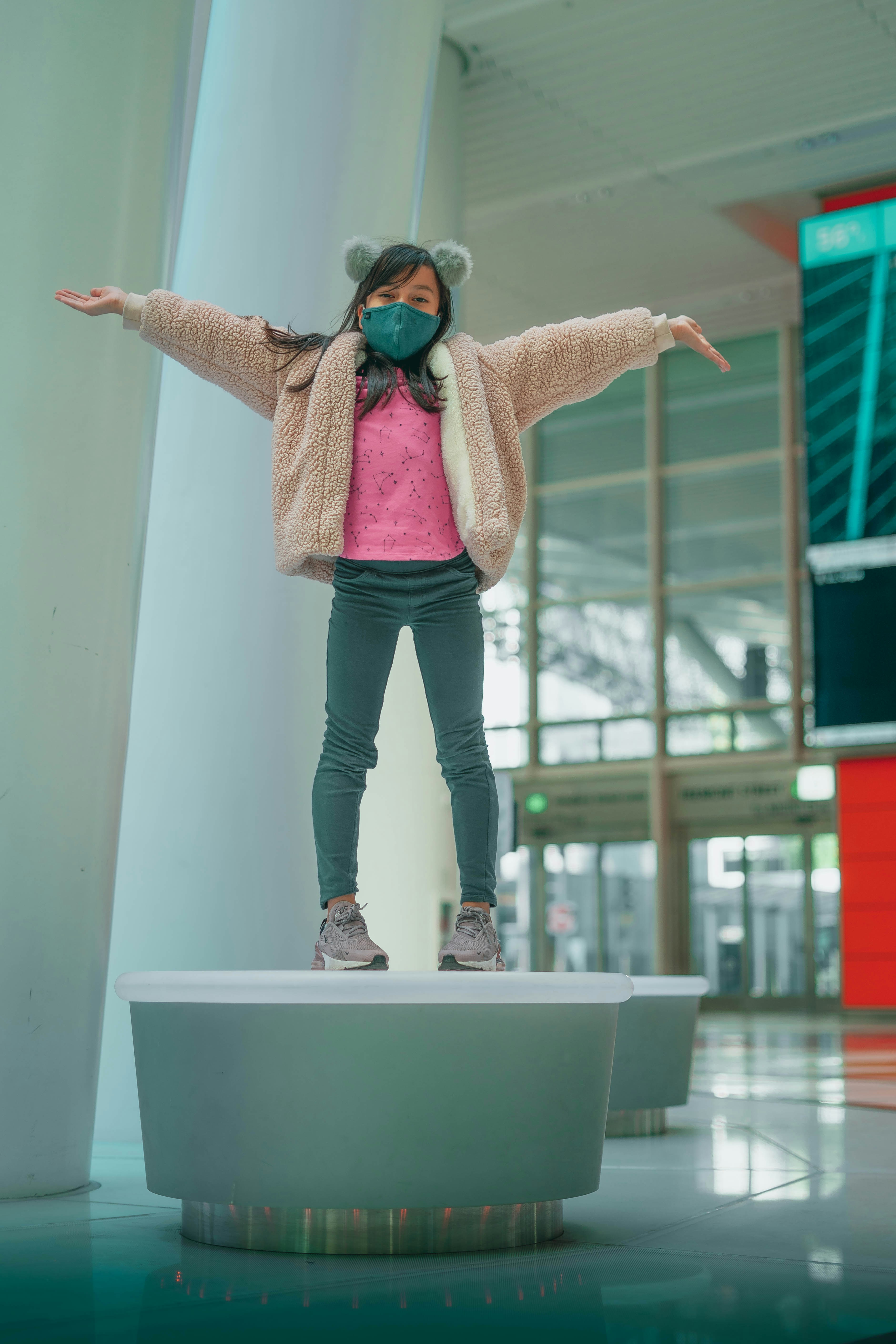 woman in brown cardigan and black pants standing on white concrete wall during daytime